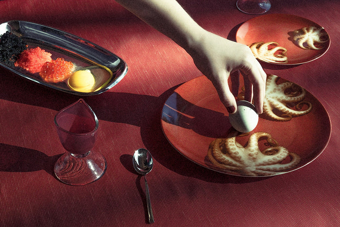Hand placing egg on dinner plate next to a platter with caviar